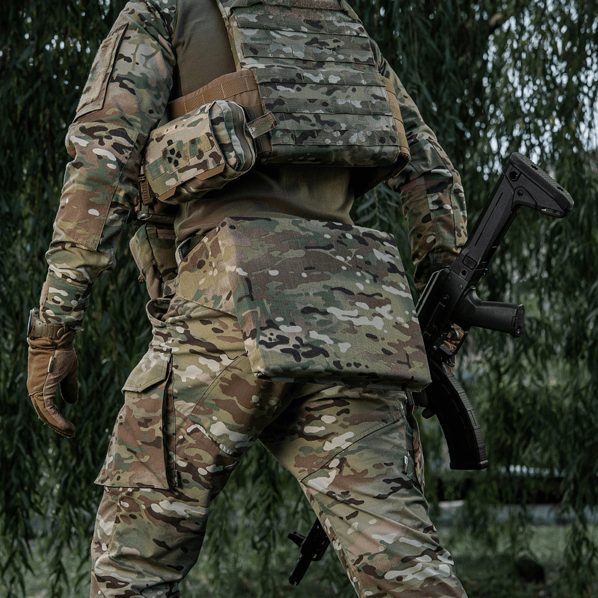 Soldat iført M-Tac Siddeunderlag med Bælte – Multicam til maksimale komfort og beskyttelse i felten, omgivet af natur.