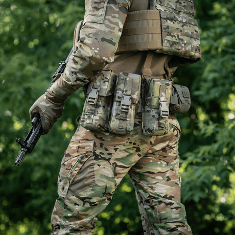 Mand i camouflageudstyr iført M-Tac Dobbelt Magasin Taske med Fastex Lukning, klar til militær og sikkerhedsaktiviteter i skoven.