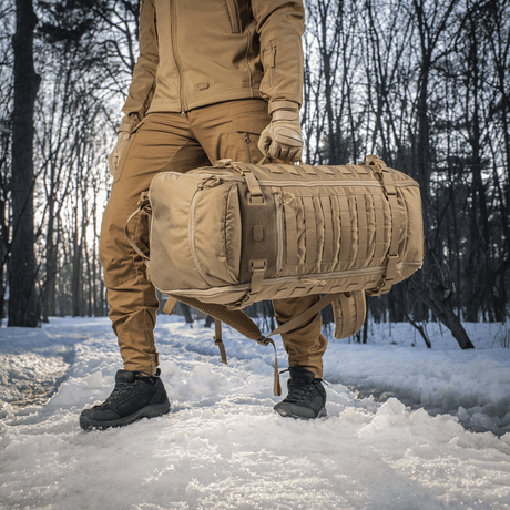 Person bærer M-Tac Rygsæk Gen.II Elite Large i sneklædt skov, fremstillet af slidstærk Cordura med stilrent design.