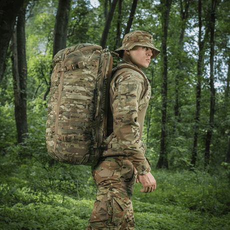 Person i skov med camouflage M-Tac Rygsæk Gen.II Elite Large, holdbar taske til udendørs eventyr.