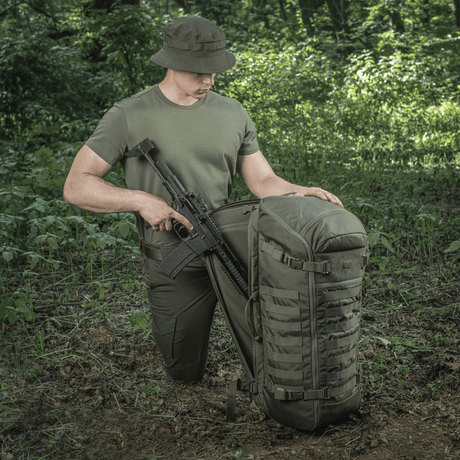 M-Tac Rygsæk Gen.II Elite Large i skoven med våben, viser holdbar konstruktion og funktionalitet til udendørs eventyr.