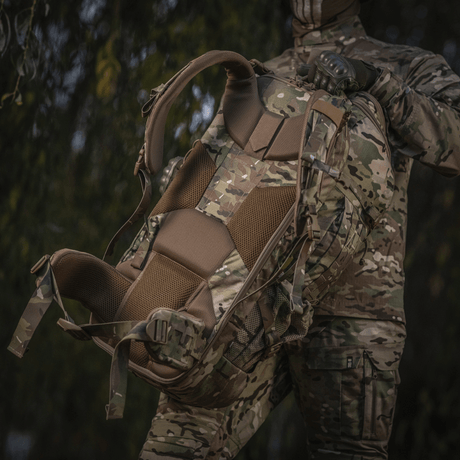 M-Tac Rygsæk Large Gen.IV Elite i camouflagemønster, ergonomisk design, holdt af person i militærtøj i naturmiljø