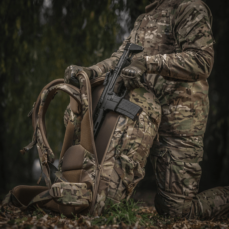Person med camouflage holder våben og M-Tac Rygsæk Large Gen.IV Elite i skovområde.