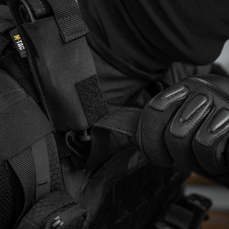 Person iført sort beskyttelsesudstyr bruger M-Tac Tourniquet Pouch Elastisk med MOLLE Gen.II fastgjort til vesten