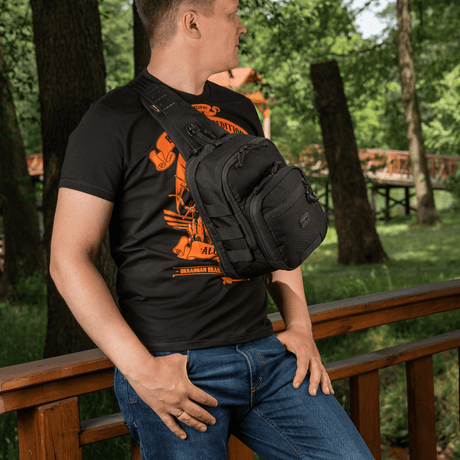 Mand bærer M‑Tac Cross Bag Elite Hex sling pack på en bro i skoven, perfekt til dagligt brug. Tasken rummer op til 5 liter.