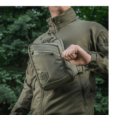 Person iført M-Tac Sling Pistoltaske Elite Hex udendørs i komfortabel og holdbar taske med justerbar rem og rummelige rum.