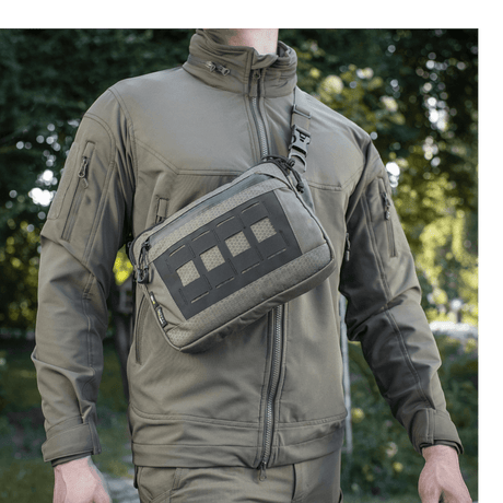 M-Tac Admin Taske Elite bæres af en person i skovmiljø, lavet af slidstærkt Cordura 500D og Hex med kvalitetslynlåse.