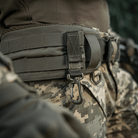M-Tac Karabinhage Tilbehør fastgjort på camouflageret taktisk bælte med MOLLE-system, komplementeret af justerbar Velcro-rem.