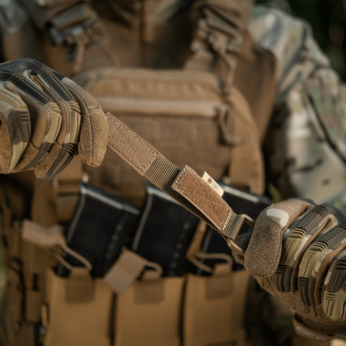 Person, der demonstrerer brug af M-Tac Fastgørelse med D-ring på taktisk vest med MOLLE-system i udendørs miljø.