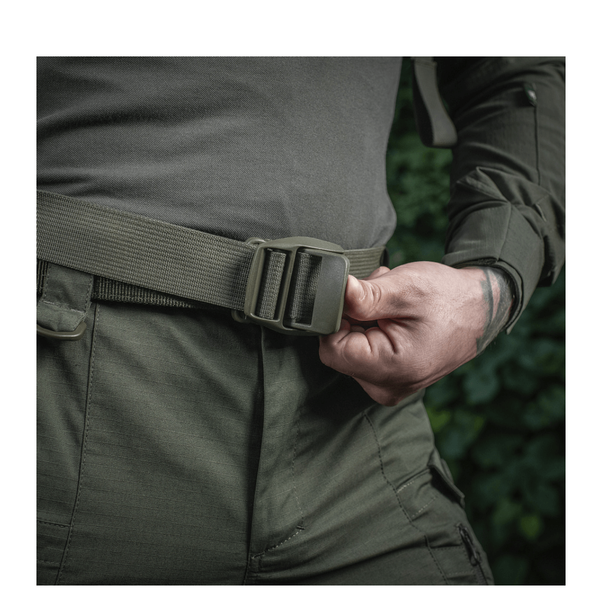 Person justerer bælte på M-Tac Mission Rygsæk Elite Hex for øget komfort og sikkerhed i udendørs omgivelser.