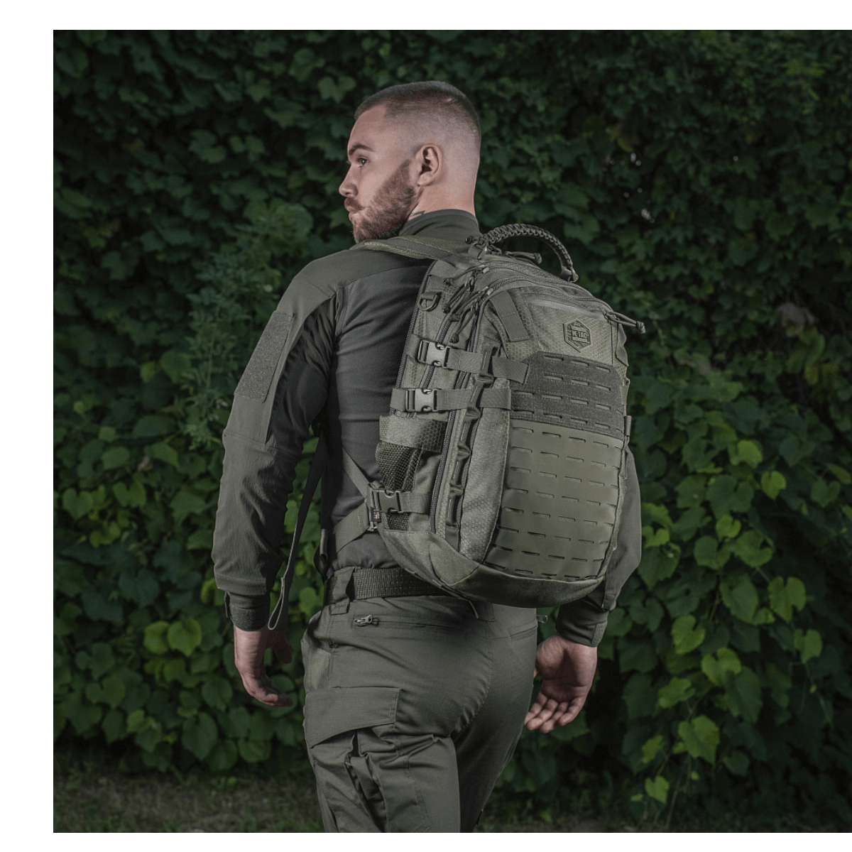 Mand iført M-Tac Mission Rygsæk Elite Hex med ergonomisk design og Cordura Hex 1000D materiale, set bagfra mod grøn baggrund.