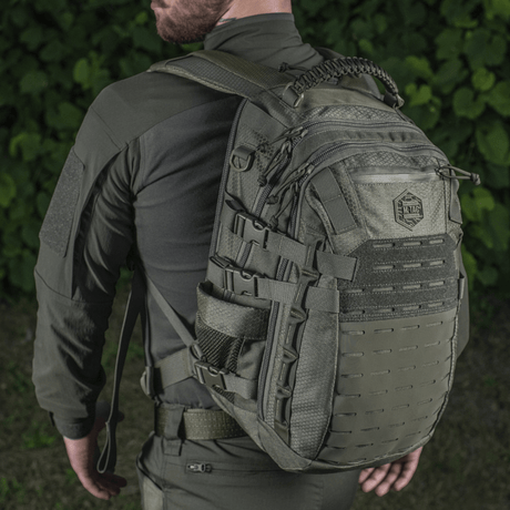 M-Tac Mission Rygsæk Elite Hex på ryg af person i taktisk tøj, med Cordura materiale og MOLLE system, set bagfra i naturen.