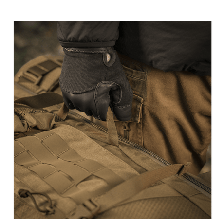 Bruger iført handsker holder M-Tac Rygsæk Large Elite Hex Gen. IV, lavet af slidstærkt Cordura 500D og Hex 1000.