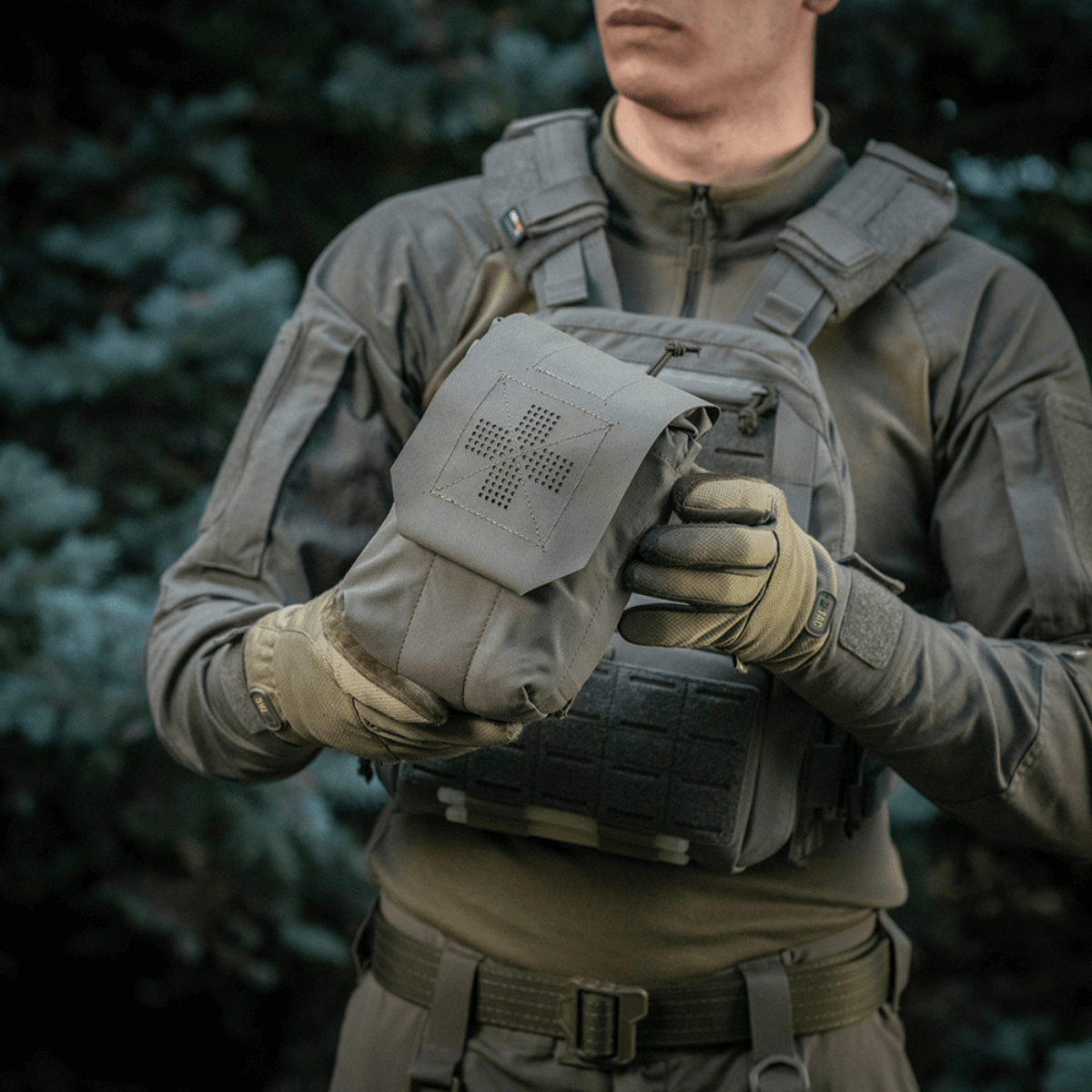 Person holder M‑Tac Medic Pouch Vertical Large Elite i skovmiljø, viser taske med holdbar Cordura 500D materiale til førstehjælpsudstyr.