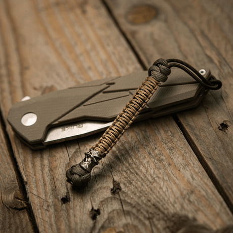 M-Tac Knife Lanyard Ninja i paracord ved siden af foldekniv på træbord.