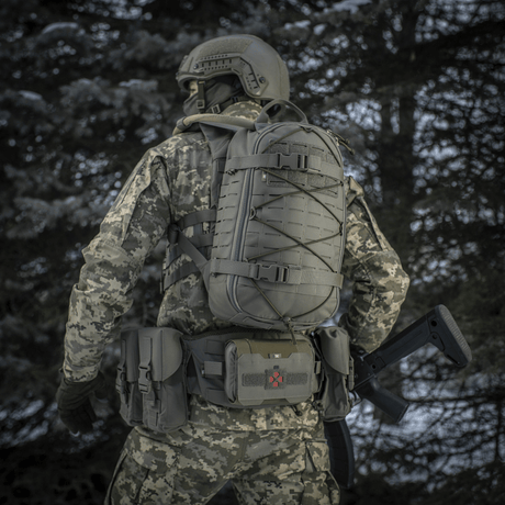 Taktisk person med M-Tac Rygsæk Sturm Elite Gen.II i et skovmiljø iført camouflage uniform, set bagfra