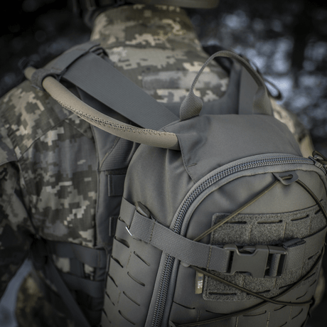 M-Tac Rygsæk Sturm Elite Gen.II i gråt Cordura stof på soldat iført camouflage, viser indbygget drikkesystem med slange i naturen.
