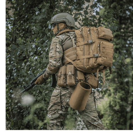 M-Tac Large Assault Pack Rygsæk i brug af en person i camouflagetøj i skovmiljø, med MOLLE-system og justerbare skulderremme.