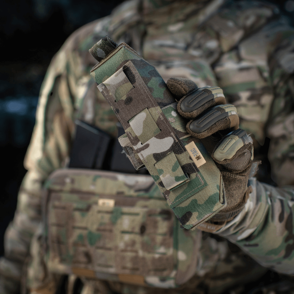 M-Tac Lomme til Tourniquet Closed i camouflage mønster, holdt af en person i militæruniform for førstehjælp i nødsituationer.