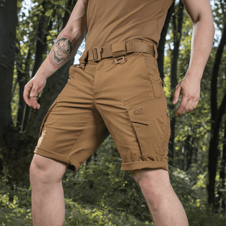 M-Tac Shorts Aggressor Gen.II Flex i brun farve, holdbare rip-stop materiale, perfekt til træning og fritid, vist i skovmiljø.