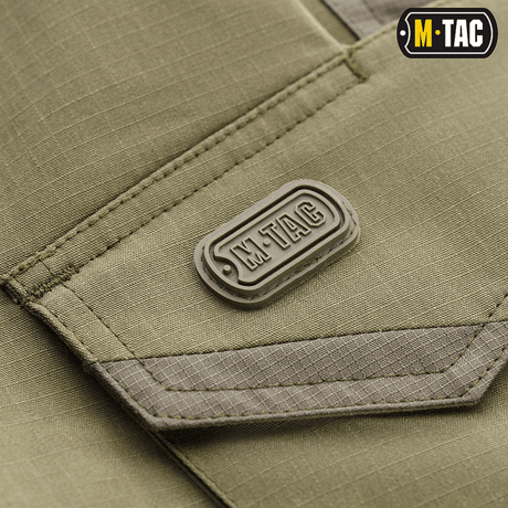 Nærbillede af M-Tac Shorts Aggressor Short i olivengrøn, viser mærke og detaljerne i rip-stop materiale, ideel til taktisk brug.