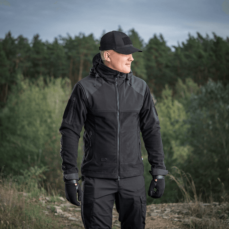 Mand iført M-Tac Norman Windblock Fleecejakke i skovområde, ideel til kulde og vind, viser jakke funktionalitet og design.