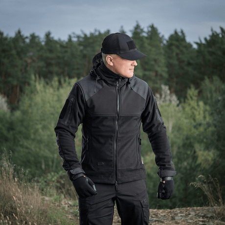 Mand iført M-Tac Norman Windblock Fleecejakke står udendørs i skovområde, ideel til overgangsperioder og kolde forhold.