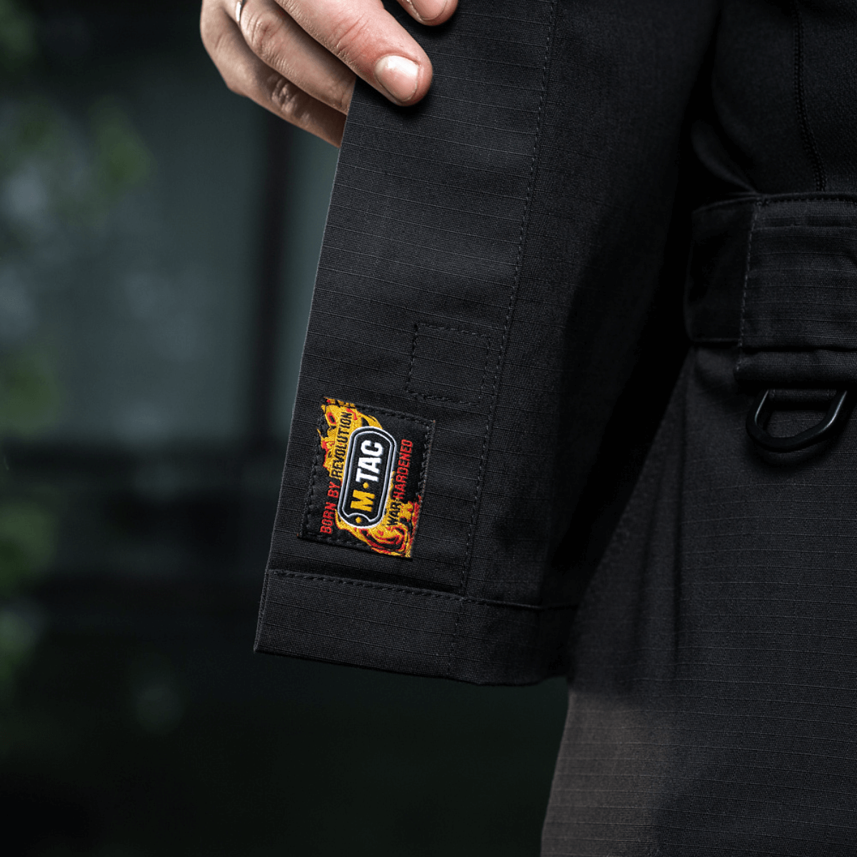 Hånd ved lomme på sort M-Tac Jakke Patrol Flex med Velcro-logo på ærme, detaljer viser taktisk design.