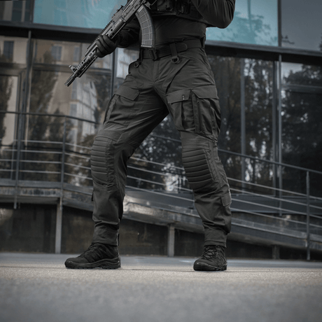 Mand iført M-Tac Bukser STURM NyCo Extreme Gen.II med våben foran moderne bygning