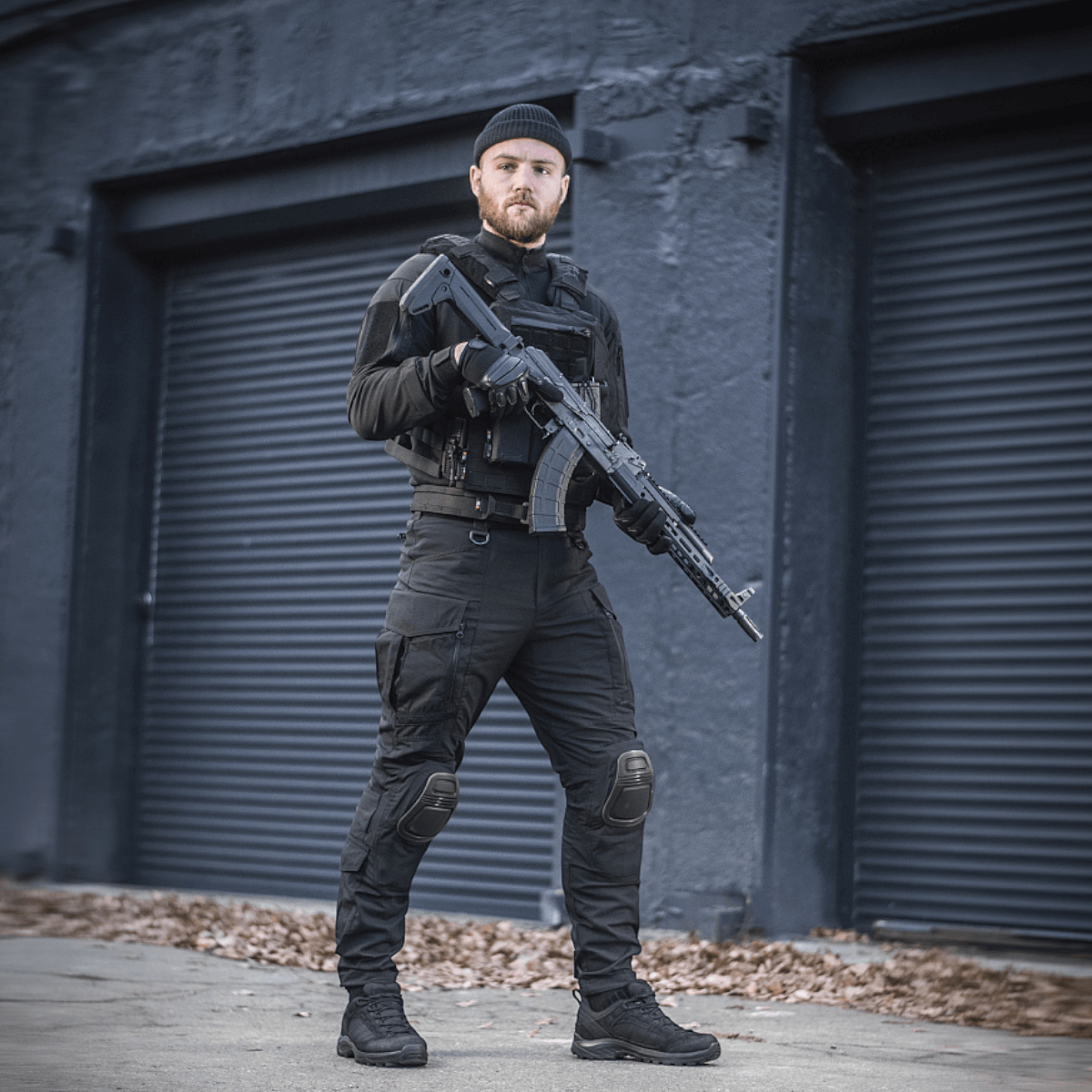 En person iført M-Tac Bukser Army NYCO Extreme i holdbart NYCO Extreme-stof, stående foran en industriel bygning.