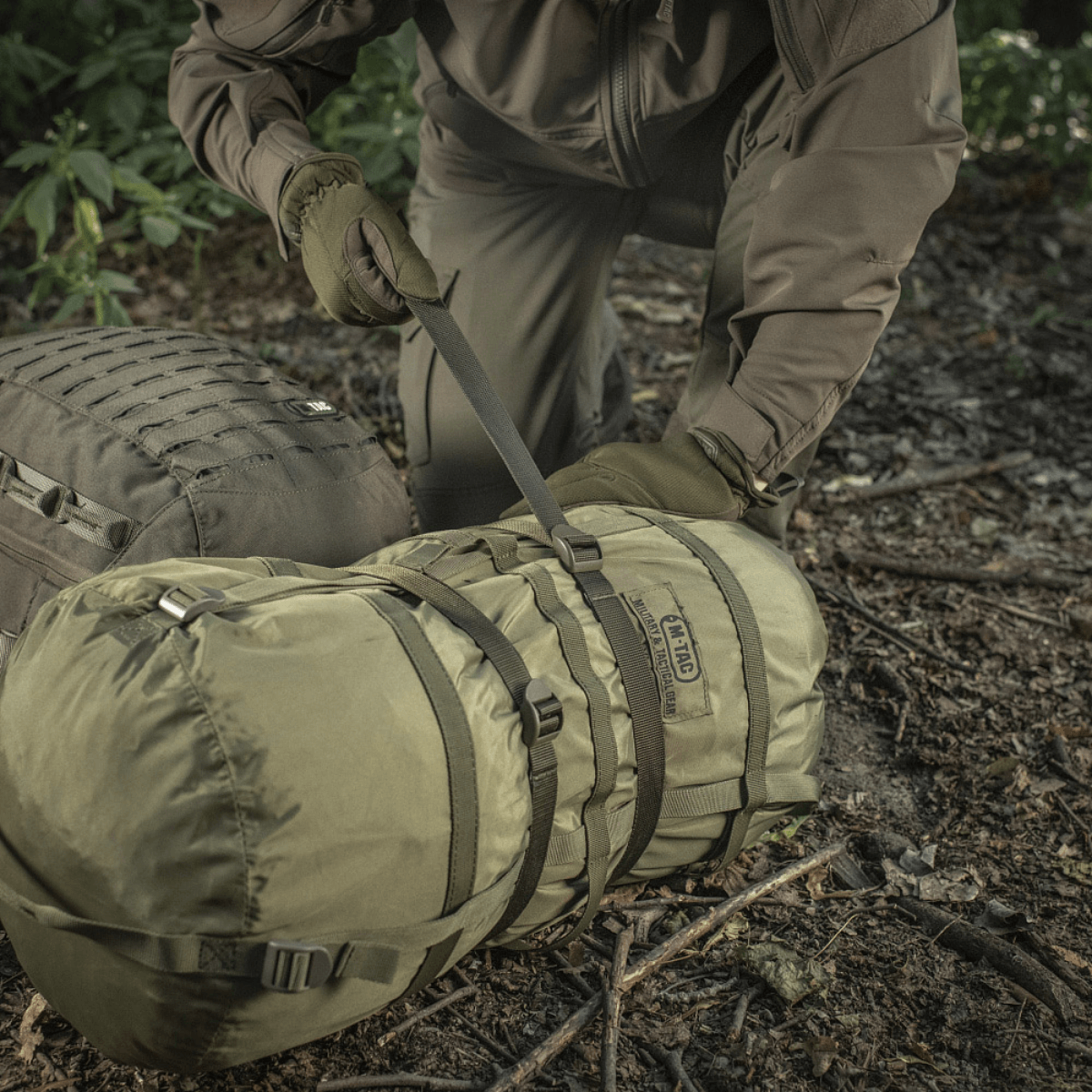 M-Tac Kompressionsrem i brug til fastgørelse af ekstra udstyr på en rygsæk under en vandretur i skoven.