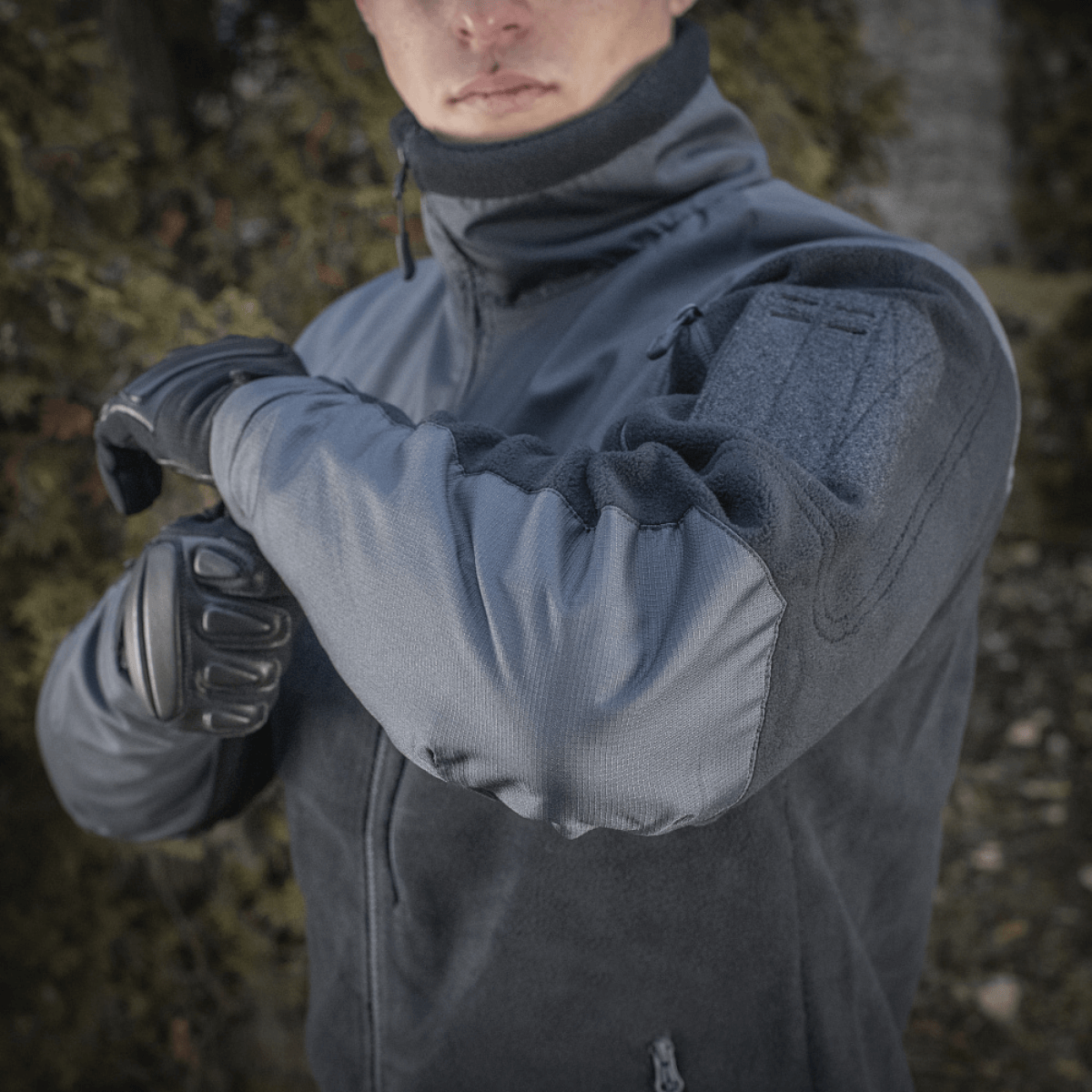 M-Tac Alpha Microfleece Jakke Gen.II i naturen, designet til taktisk og outdoor-brug med forstærket slidstyrke på skuldre og ærmer.