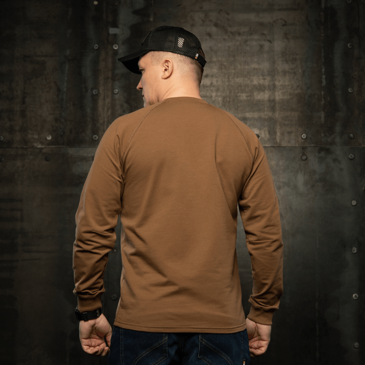 Mand iført M-Tac Raglan Athlete sweatshirt med raglanærmer i coyote-farve, set bagfra mod industriel baggrund.