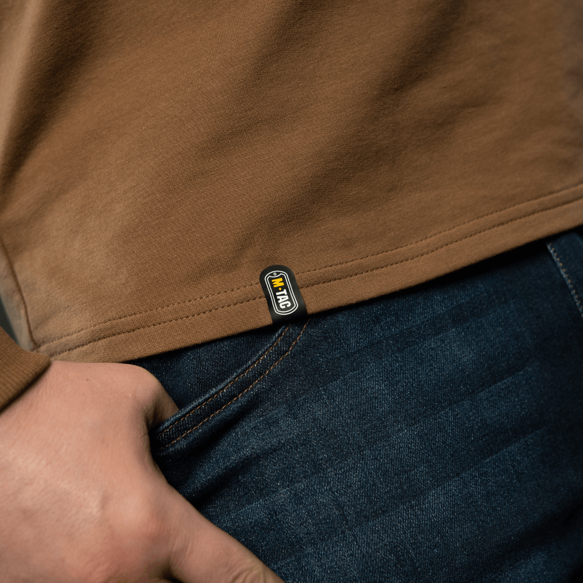 Close-up af M-Tac Raglan Athlete sweatshirt i coyote farve, fremhæver detaljerne og logoet ved kanten.