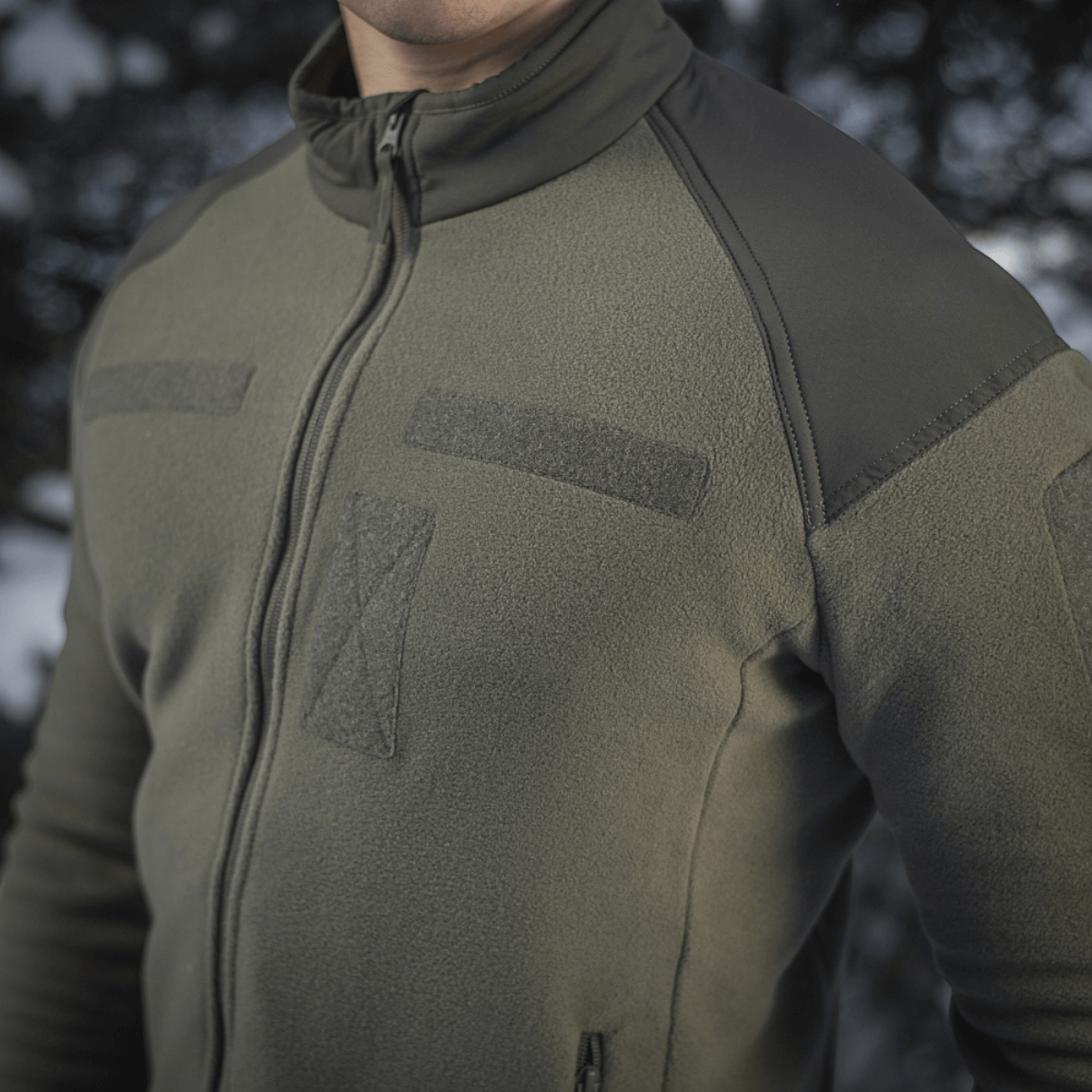 M-Tac Combat Fleece Jakke i grøn med vindtæt design, set i udendørs omgivelser. Perfekt til varme og åndbarhed.