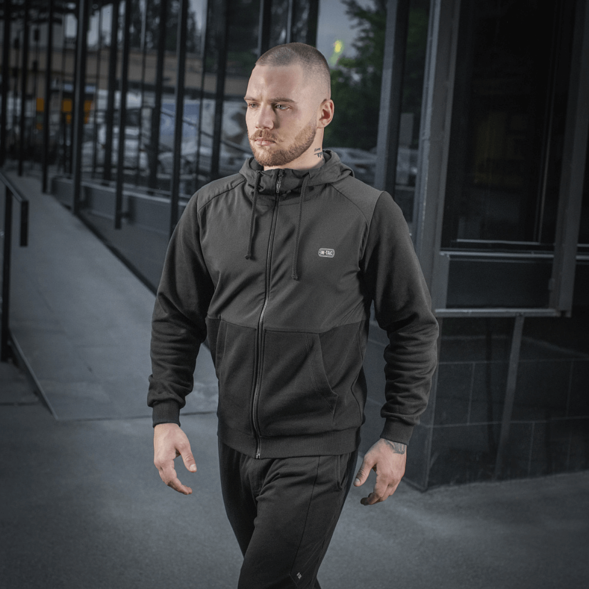 Mand iført sort M-Tac Pilgrim Bomberjakke går på gaden, fremhæver stilfuld og praktisk design, ideel til hverdagsbrug.