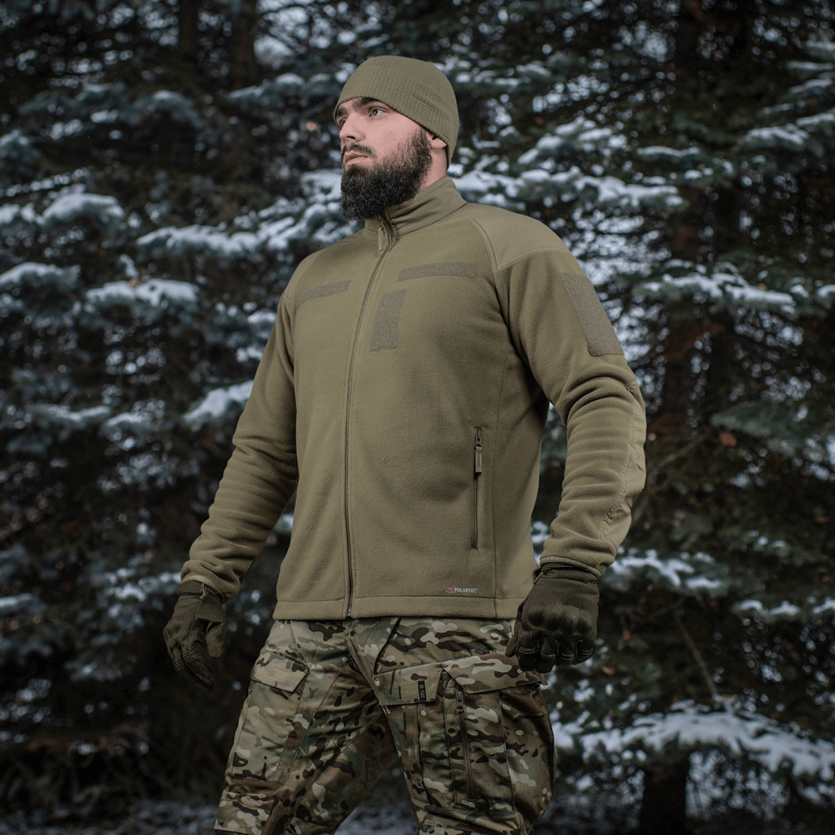 Mand iført M-Tac Combat Fleece Polartec Jakke i snedækket skovmiljø, ideel til taktisk og casual brug.