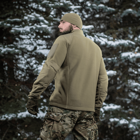 Person iført en M-Tac Combat Fleece Polartec Jakke i skov, set bagfra. Perfekt til både taktisk og casual brug.