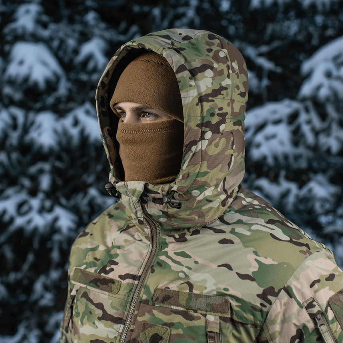 Person iført M-Tac Alpha Gen.IV Pro Primaloft Vinterjakke i sneklædt skov, camouflage design for ekstrem beskyttelse ned til -20°C.