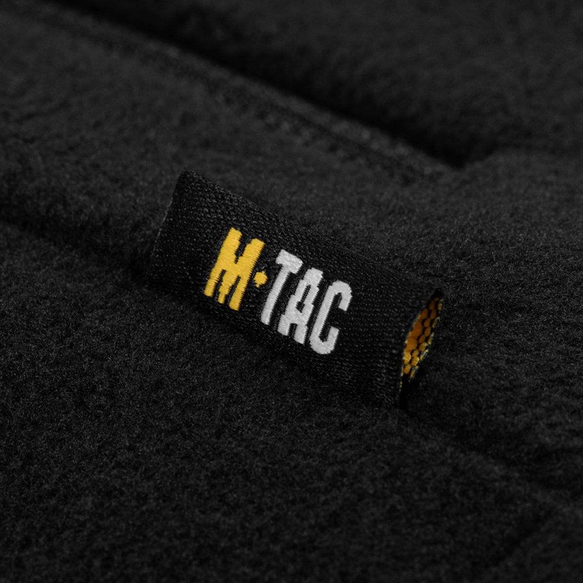 Tæt på lædermærke på M-Tac Combat Fleece Jakke Polartec Dame med sort fleece baggrund, fremhæver høj kvalitet og robust design.