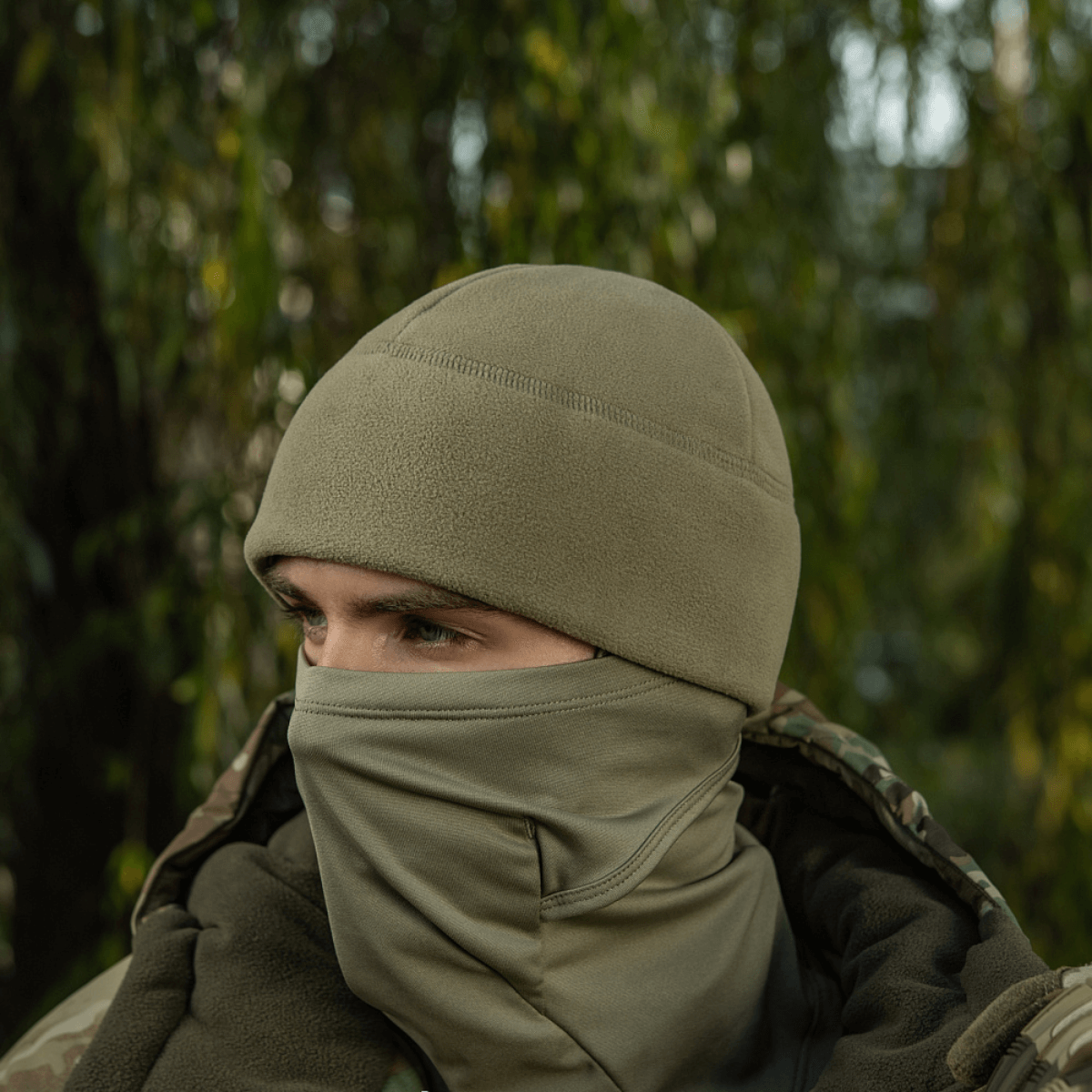 Person iført M-Tac Watch Cap Elite Fleece Beanie Hat Slimtex i natur, ideel til koldt vejr og taktisk brug med camouflagejakke.