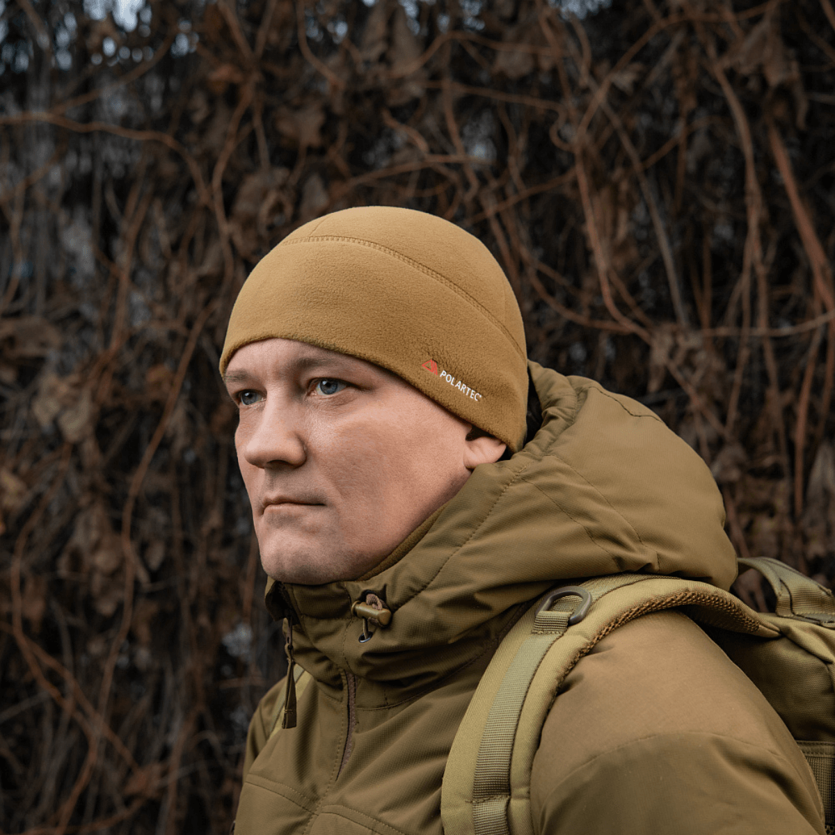 Mand iført M-Tac Fleece Watch Cap Light Polartec hue i brune toner, velegnet til vinterbeskyttelse mod kulde og vind.