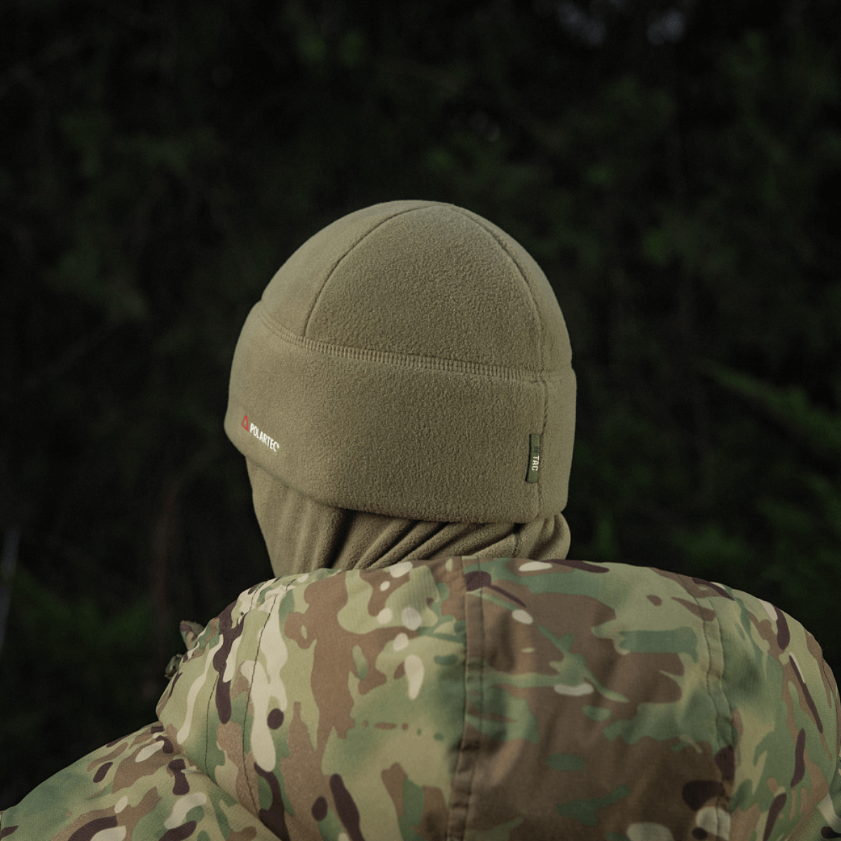 Person iført en M-Tac Fleece Polartec Watch Cap og camouflagemønster jakke i en udendørs skovscene