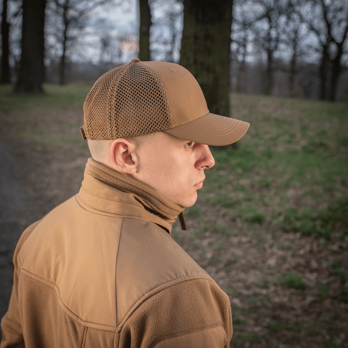 Mand bærer M-Tac Mesh Flex Ripstop Baseball Cap i skovmiljø, der viser kasketens mesh-paneler og holdbare skygge.
