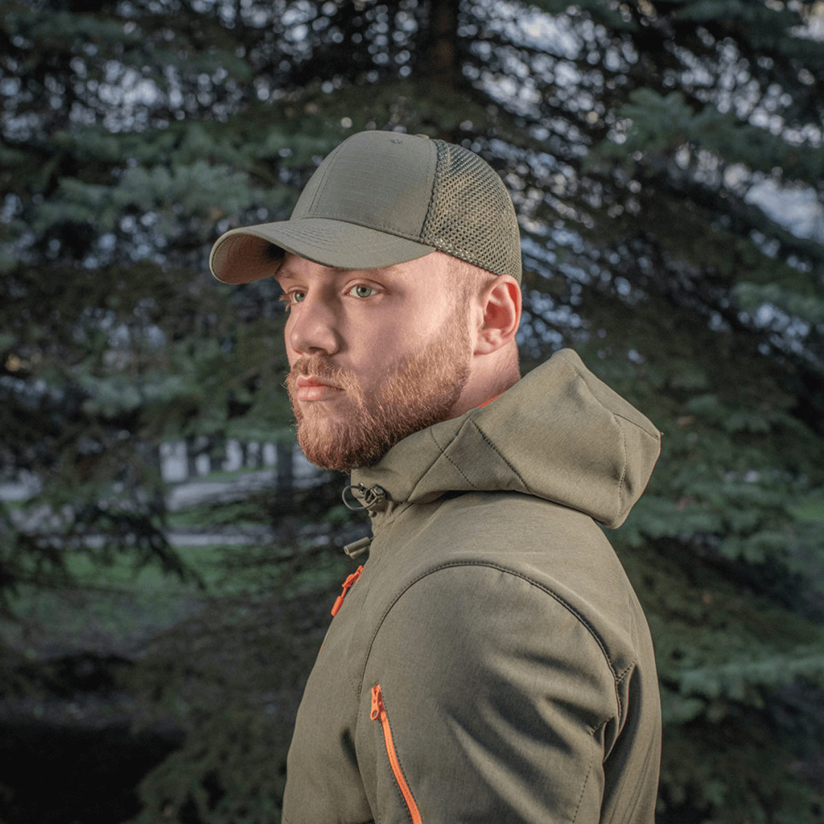 Mand iført M-Tac Mesh Flex Ripstop Baseball Cap i grøn, stående foran et træ i en udendørs setting.