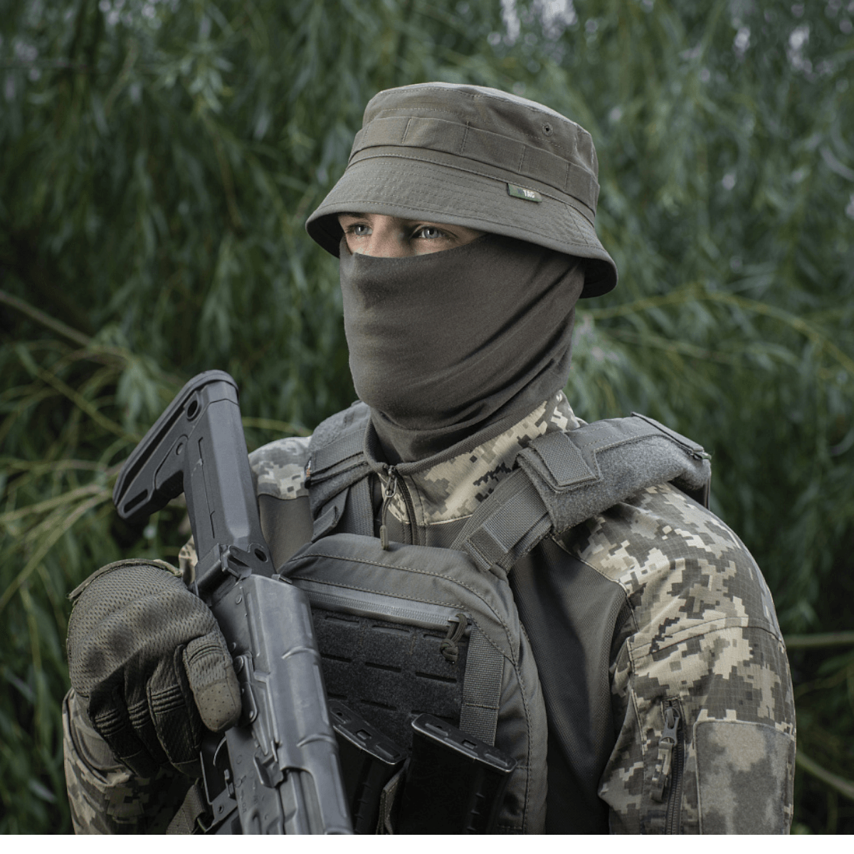 Person iført M-Tac Panamahat Gen. II Flex Rip-Stop med maskering, camouflageudstyr i skovmiljø.