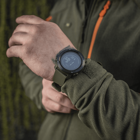 M‑Tac Multifunktionelt Taktisk Ur med elektronisk kompas og 3D pedometer set på en hånd, ideel til friluftsliv og militærbrug.
