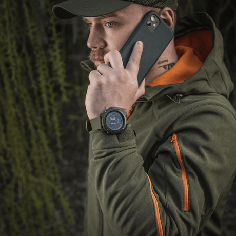 Mand iført M‑Tac Multifunktionelt Taktisk Ur mens han taler i telefon, skovbaggrund.