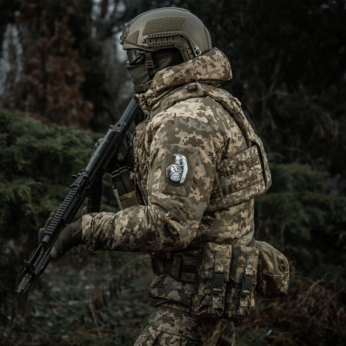 Soldat i camouflageuniform med M-Tac Patch M67 Granat 3D PVC på ærmet, bevæbnede i skoven.