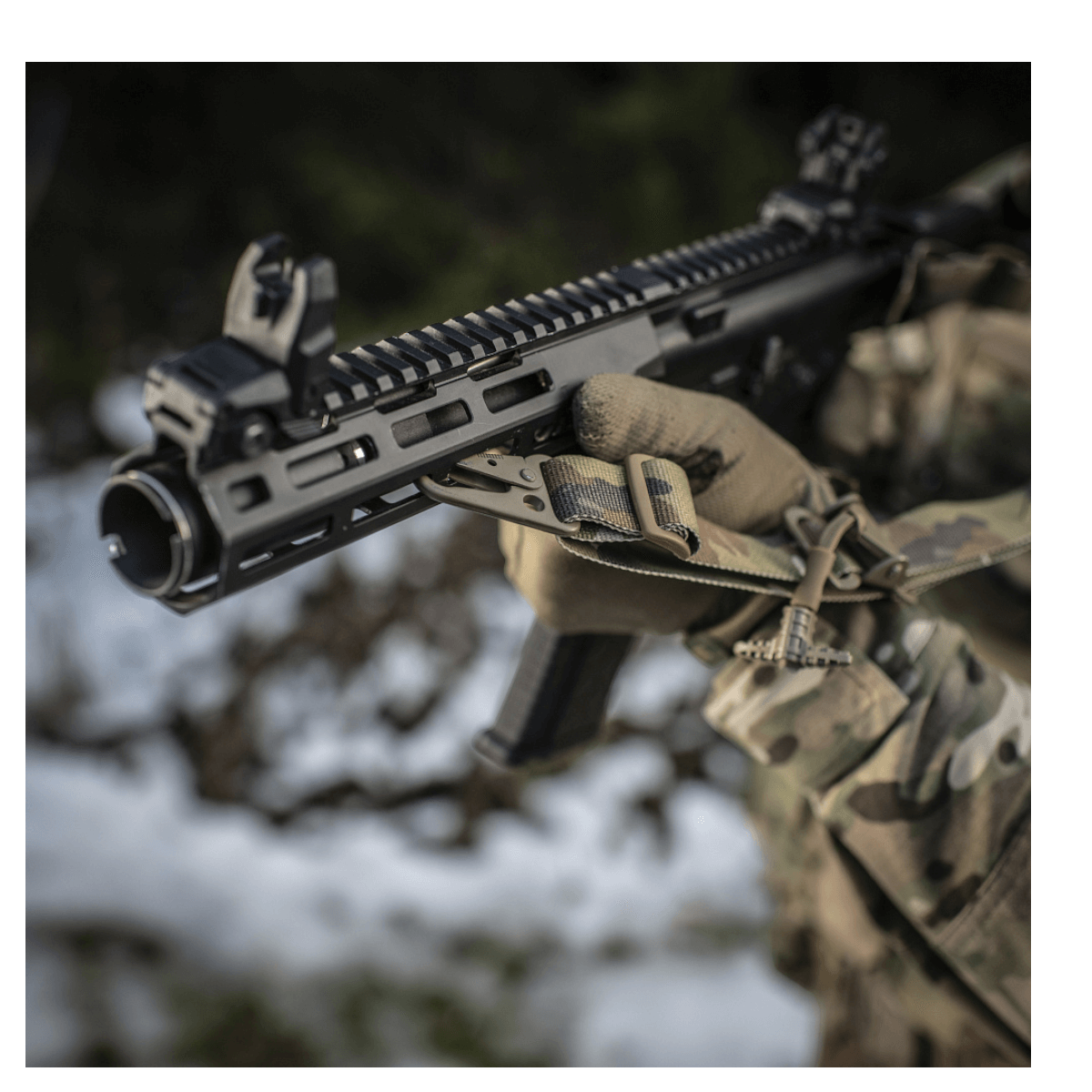 Soldat justerer M-Tac Universal Våbenrem på et gevær, der viser to-punkts fastgørelsessystem i en udendørs skovindstilling.